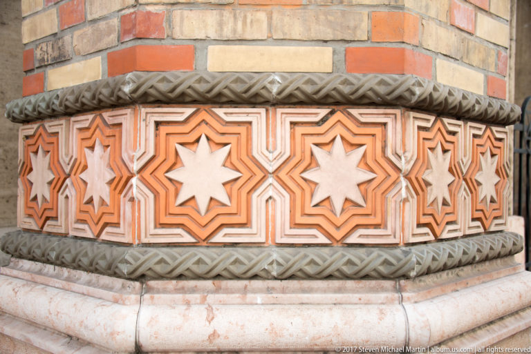 Close frieze of repeated eight-pointed stars in terracotta and cream framed by carved moldings on the synagogue.