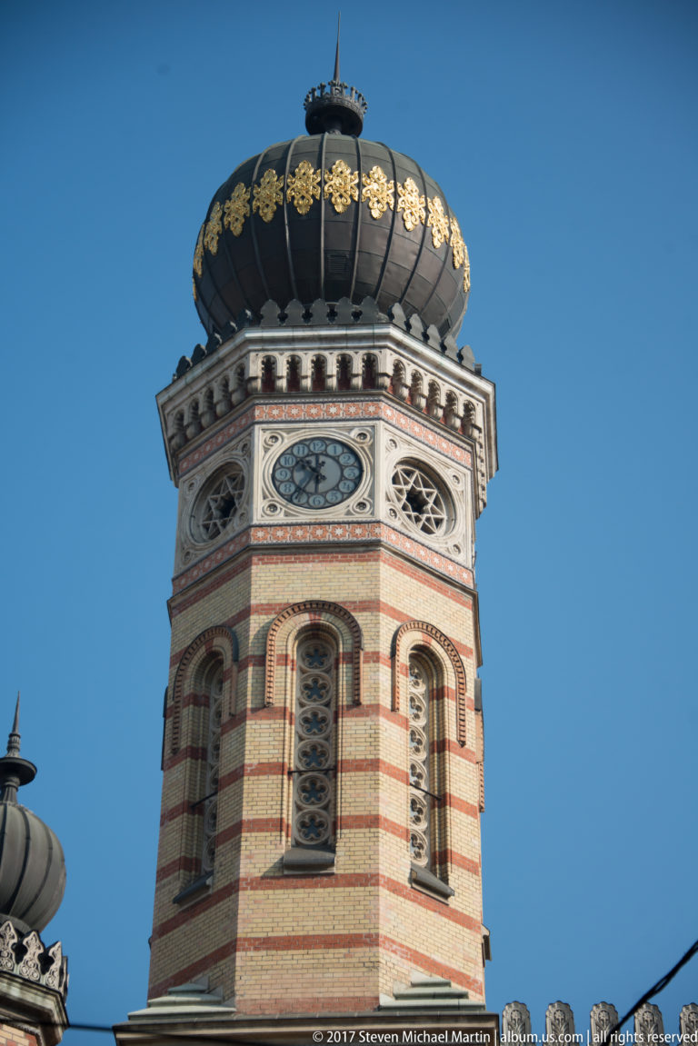 Close view of a Dohány Street Synagogue tower with striped masonry, clock face, arched windows, and dark onion dome.