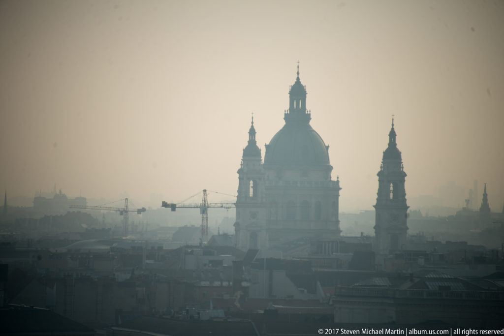 Hazy silhouette of St. Stephen’s Basilica with its central dome and twin towers rising above Budapest rooftops.