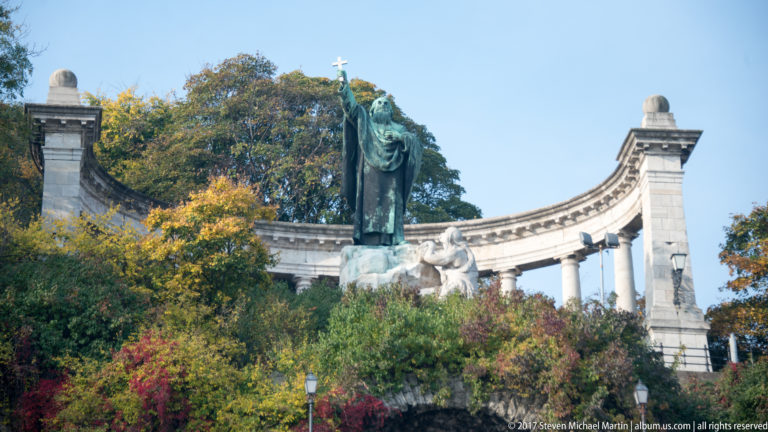 Saint Gerard monument on Gellért Hill, with robed bronze figure raising a cross before a curved stone colonnade.