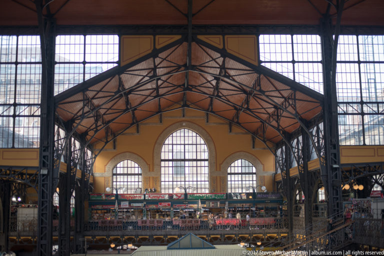 Great Market Hall interior with dark iron roof trusses, large arched windows, and an upper gallery lined with stalls.