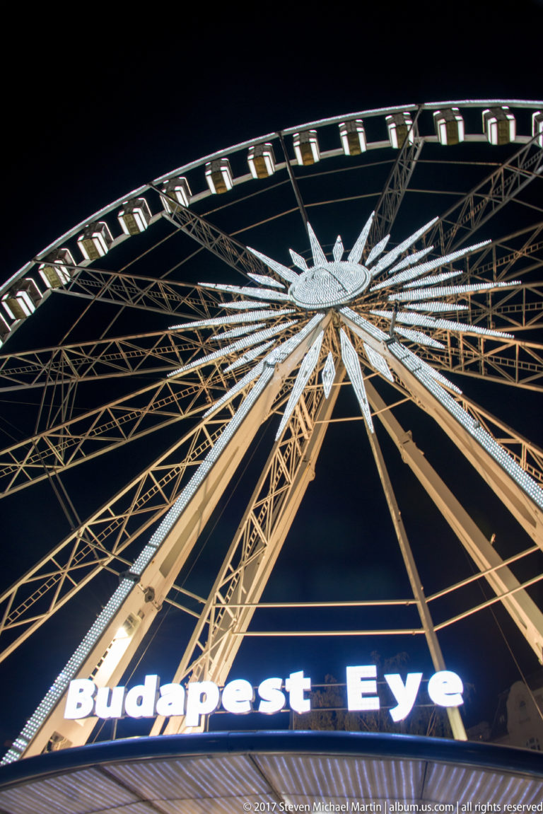 Low-angle night view of the illuminated Budapest Eye Ferris wheel with its bright name sign below.