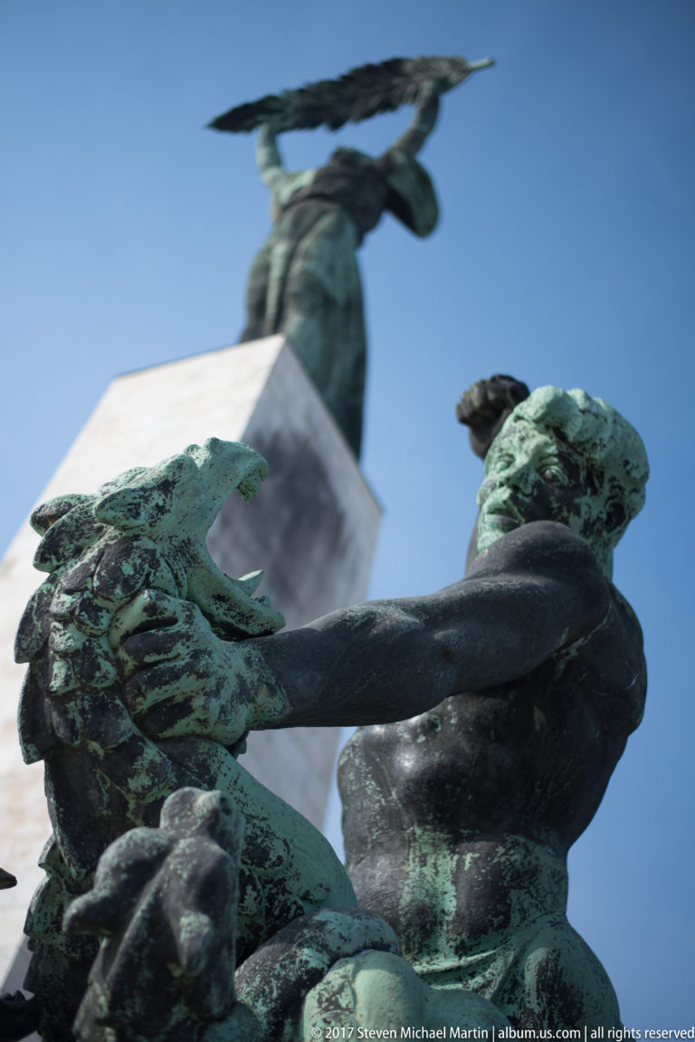 Low-angle bronze figures at Budapest's Liberty Statue monument, with the palm-bearing female figure high above.