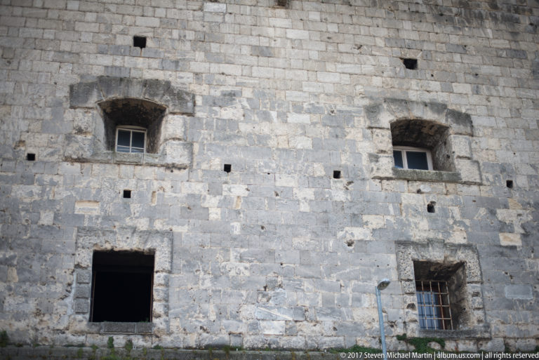 Weathered limestone Citadella wall with small openings and deep-set rectangular windows on Gellért Hill.