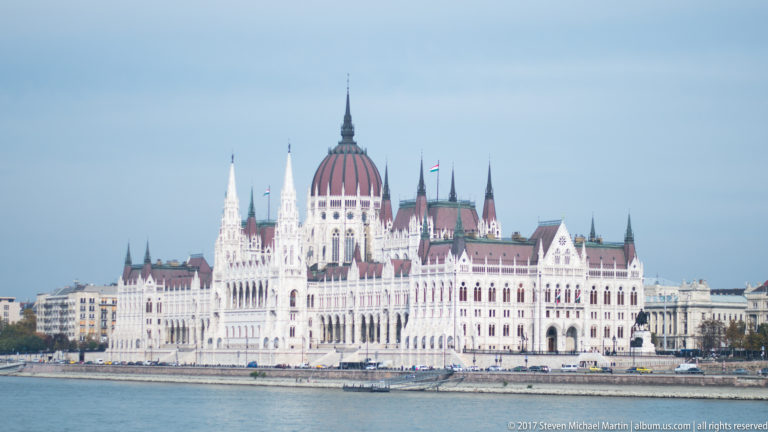 Daytime view across the Danube of the Hungarian Parliament Building with white Neo-Gothic façade and central dome.