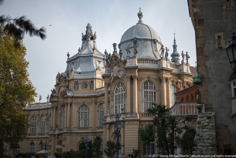Domed historicist pavilion with tall arched windows, sculptural ornament, balustrades, and pale stone façade.