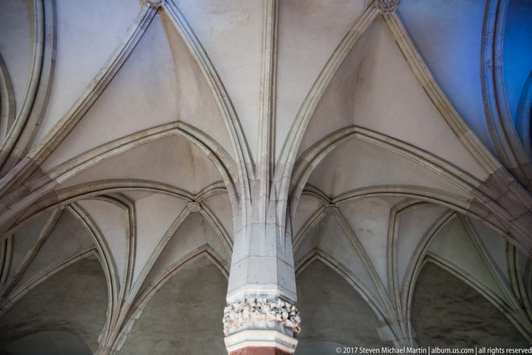 Stone ribs converging above a carved capital in a Gothic vaulted interior at Corvin Castle.
