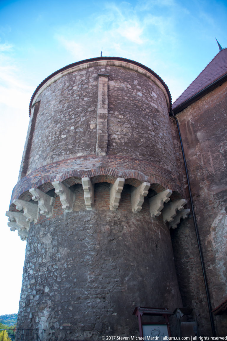 Low-angle close view of a massive round stone tower with projecting corbels and brickwork at Corvin Castle.