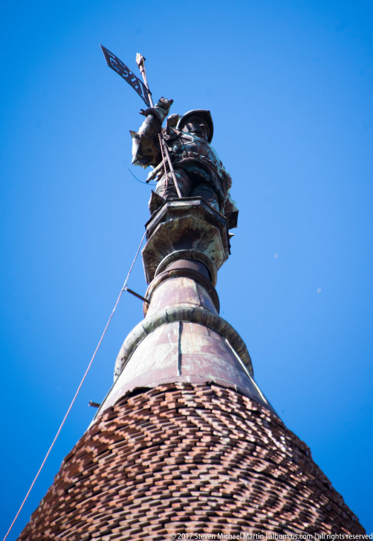 Dragon-like metal finial silhouetted above the peak of a steep tiled roof at Corvin Castle.