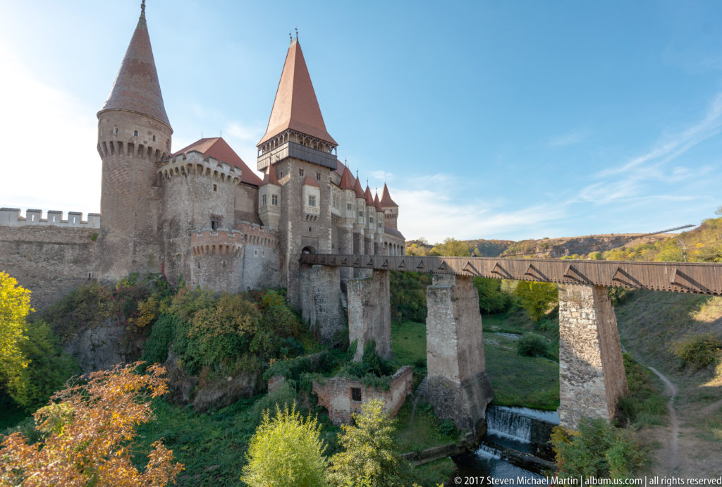 Corvin Castle above autumn vegetation with its long bridge crossing the ravine on tall stone piers.