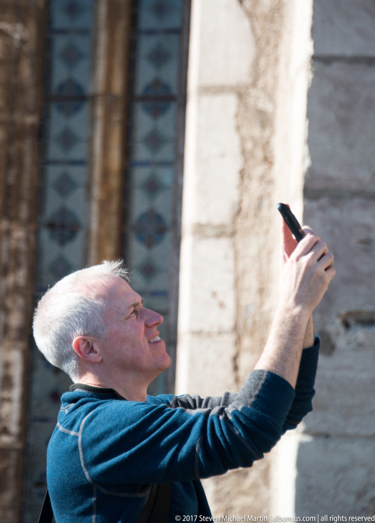 Man holding up a smartphone while photographing stone architecture and a tall window at Corvin Castle.