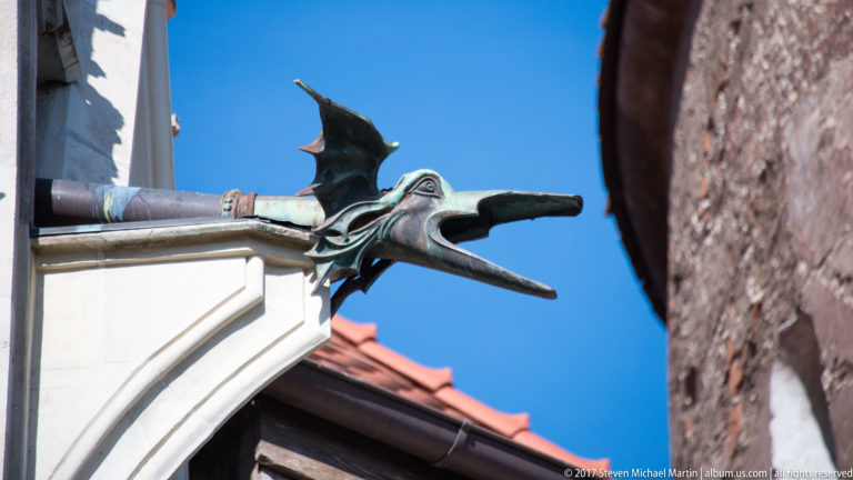 Dragon-like metal waterspout with open mouth and wings projecting from a castle roofline.