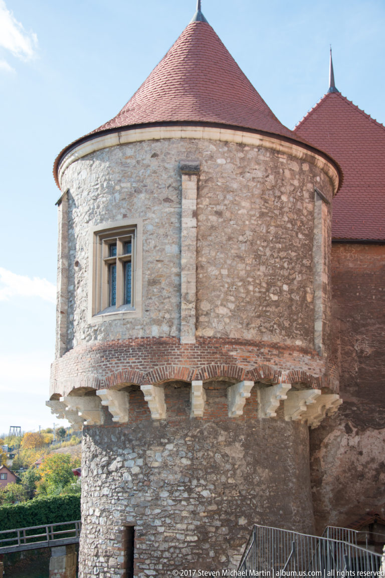 Round stone tower with small windows, projecting lower masonry, and a low conical red roof.