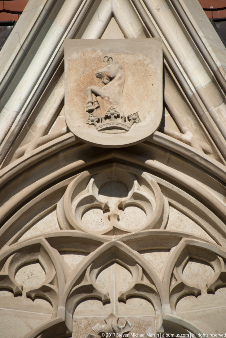 Carved heraldic shield above pale Gothic tracery and pointed stone ornament on Corvin Castle.