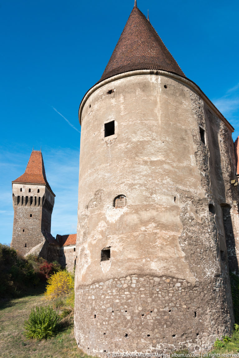 Large round stone tower with conical roof, with a square tower visible in the distance.