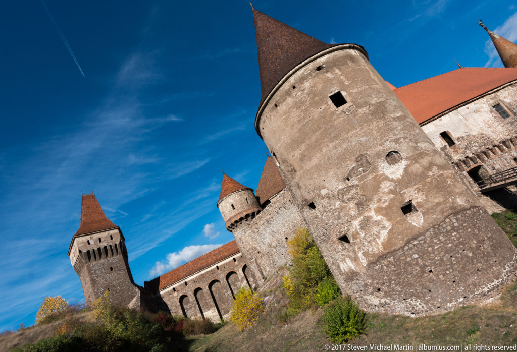 Tilted low-angle view of a round tower in front of a square defensive tower at Corvin Castle.