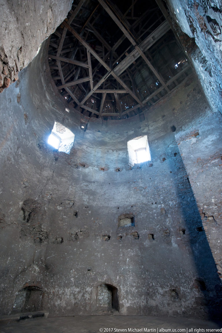 Upward interior view of a masonry tower with high windows and exposed timber roof framing.