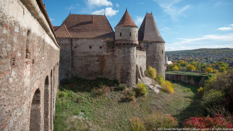 Two roofed castle towers beyond grassy lower ground, with an interior wall at left and autumn hills in the distance.