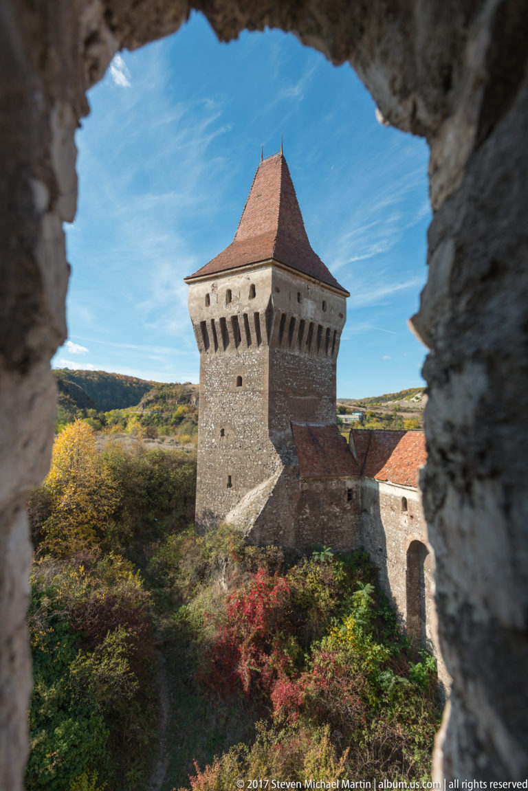 Square roofed defensive tower framed by a rough stone opening, with autumn vegetation below.
