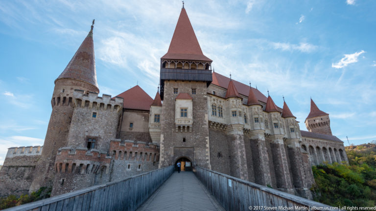 Entrance bridge leading directly to Corvin Castle’s arched gateway between round towers and a tall red-roofed gate tower.