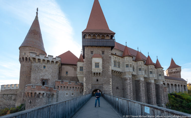 Visitor standing on the bridge before Corvin Castle’s gate tower and flanking stone towers.