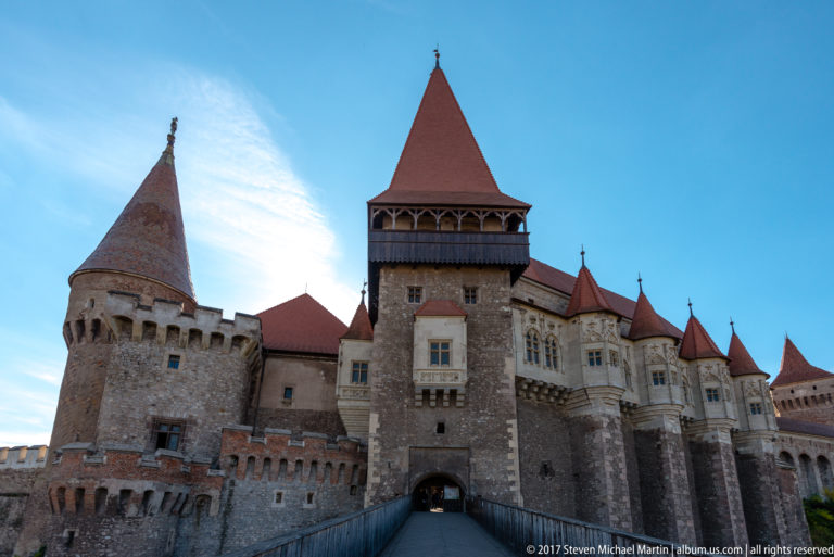 Close view of Corvin Castle’s roofed gate tower, arched passage, round tower, and projecting windows.