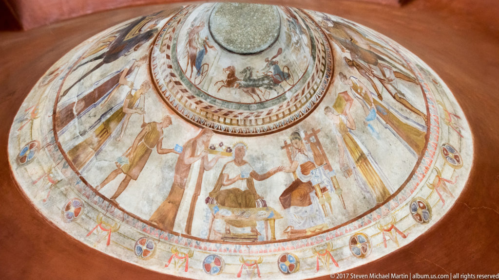 Steep oblique view of painted dome with large outer ceremonial figures below smaller concentric horse and chariot scenes.