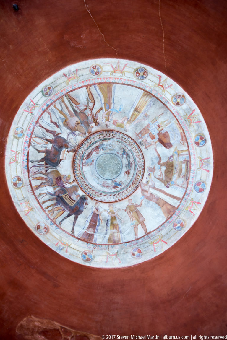 Wide low-angle view of the circular painted dome appearing elliptical against deep red plaster walls with visible cracks.