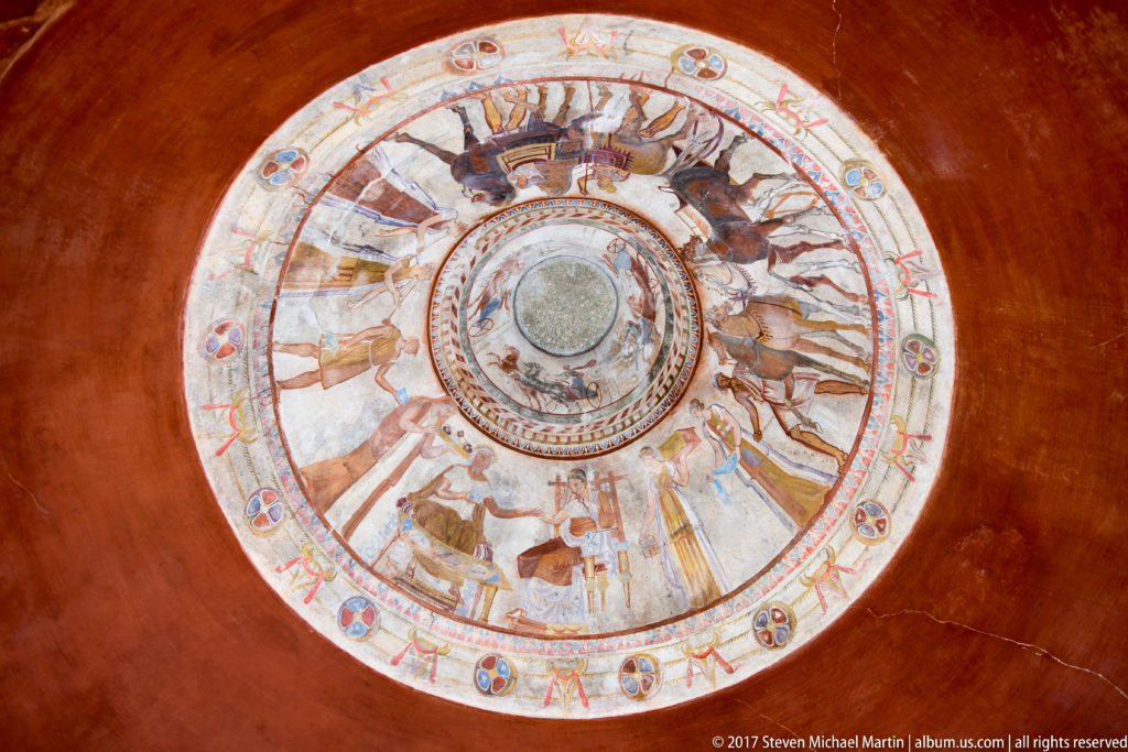 Straight-up view of a circular painted dome with central medallion, horse-and-chariot ring, outer figures, and perimeter ornaments.