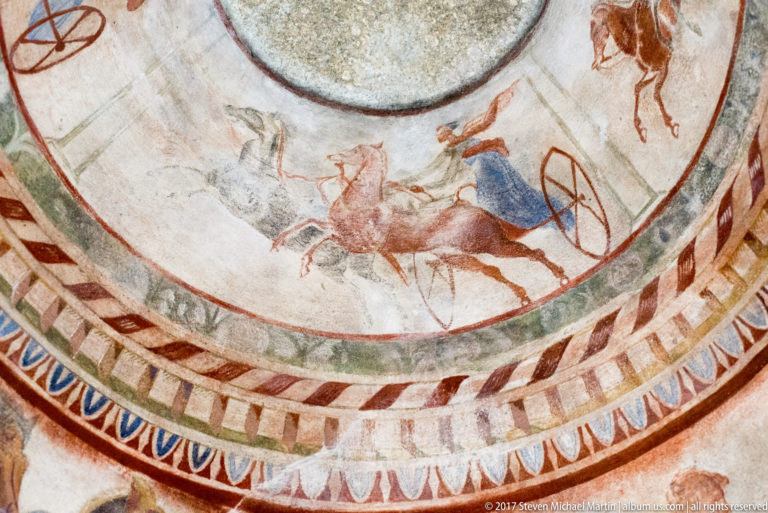 Curved dome frieze with running chariot horses, red wheel, blue-clad figure, and another horseman at upper right.
