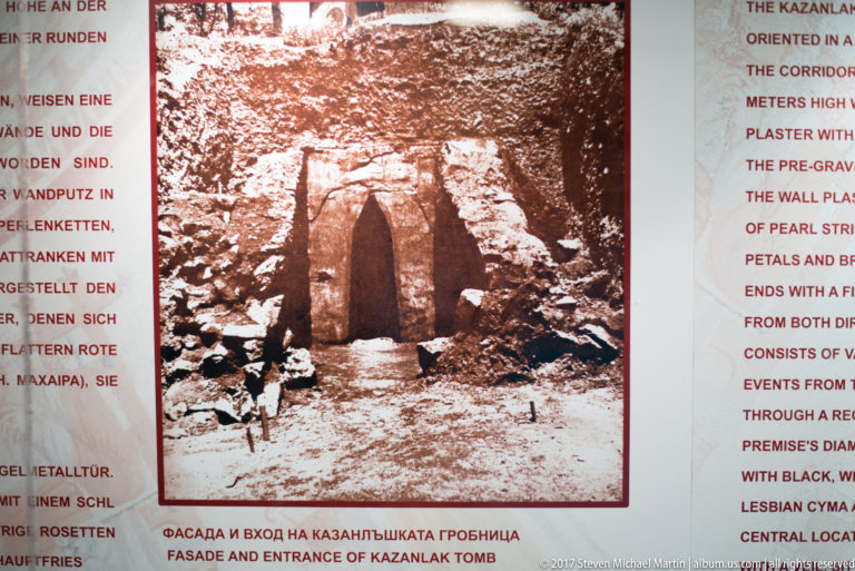 Museum panel with a historic black-and-white view of the Kazanlak tomb entrance surrounded by multilingual explanatory text.
