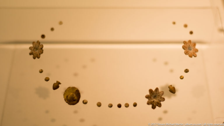 Gold-colored rosette ornaments, small round beads, and fittings arranged in a curved line on a museum display surface.
