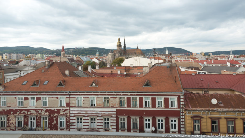 Elevated view over red-roofed central Košice with St. Elisabeth Cathedral towers rising beyond the foreground buildings.