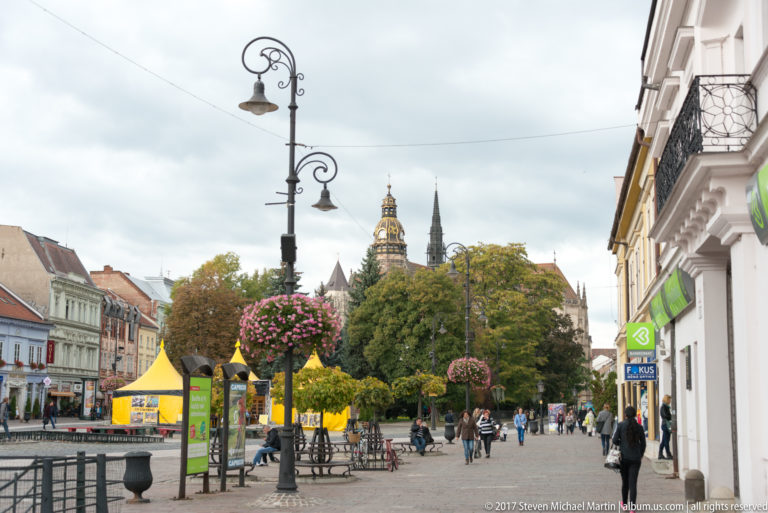 Pedestrian promenade on Hlavná ulica with flowered lamps, market tents, trees, and St. Elisabeth Cathedral in the distance.