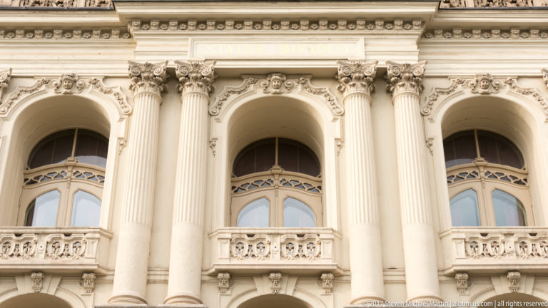 Fluted columns with ornate capitals frame arched windows and carved balconies on a richly decorated historic façade.