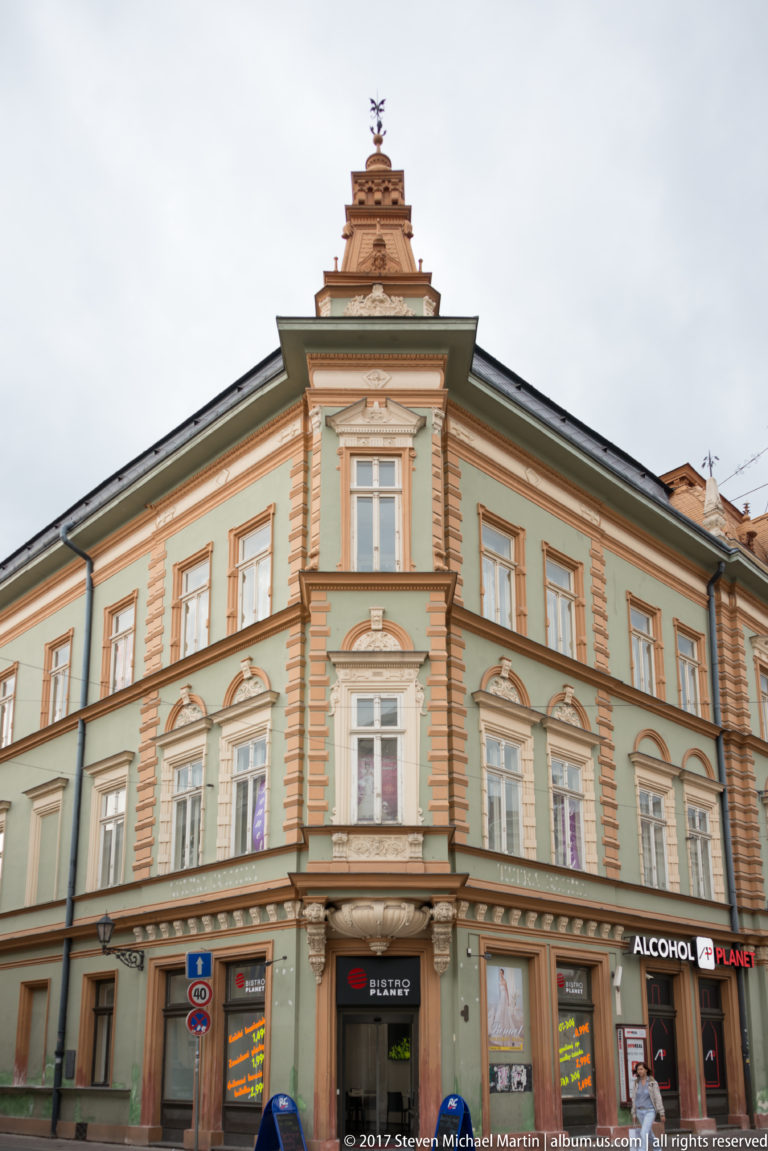 Pastel historic corner building with ornate window surrounds, pilasters, and a stepped gable above street-level shops.