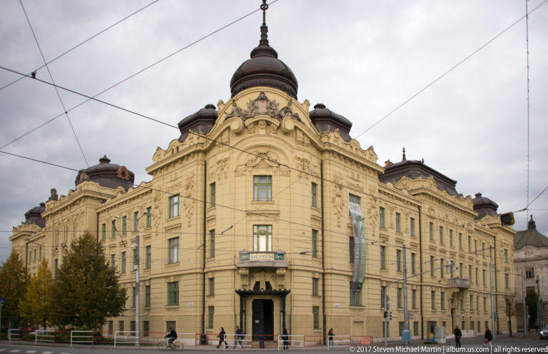 Large cream historic civic building with domed corner tower, balconies, sculpted pediments, and overhead transit wires.