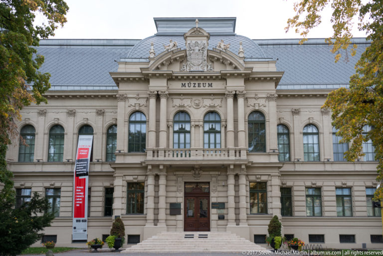 East Slovak Museum façade with central MÚZEUM inscription, arched windows, columns, sculptural cresting, and gray roof.
