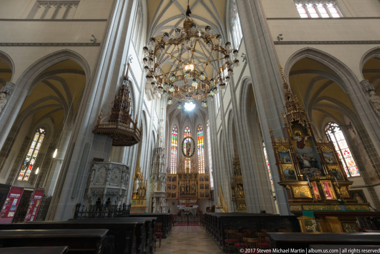 Large chandelier suspended between Gothic piers, with stained glass and richly colored altarpieces beyond in St. Elisabeth Cathedral.