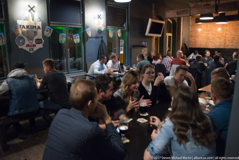 Crowded beer hall with groups of patrons seated closely together at tables during an evening gathering.