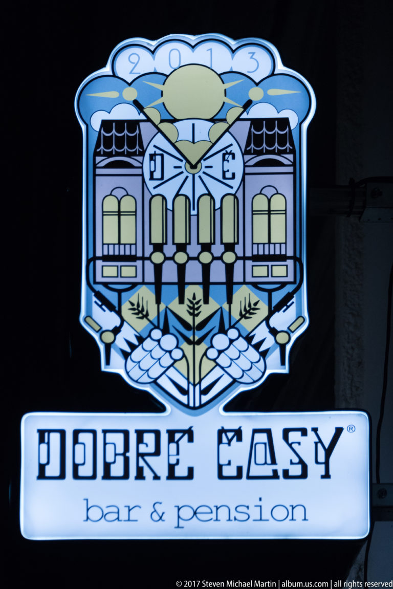 Illuminated DOBRÉ ČASY bar & pension sign with a stylized blue-and-white architectural emblem.