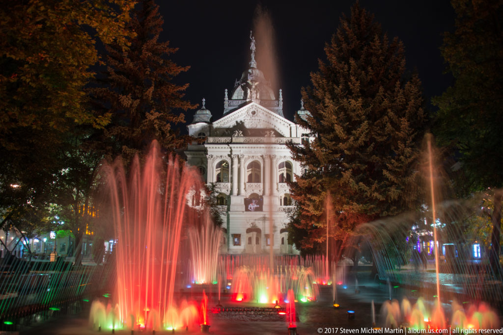 Colored fountain jets illuminated at night in front of the ornate State Theatre in central Košice.