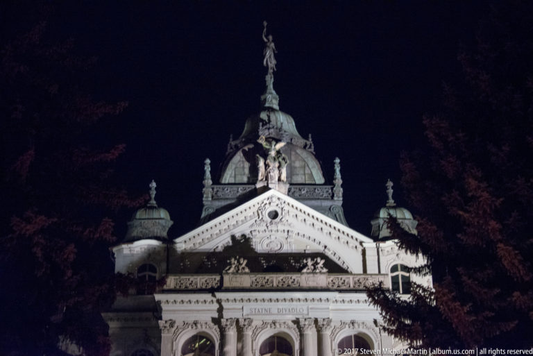 Upper State Theatre façade at night with domed roof, crowning statue, sculpted pediment, and ŠTÁTNE DIVADLO inscription.