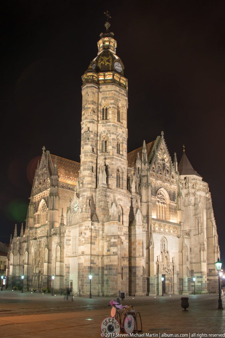 St. Elisabeth Cathedral illuminated at night, showing its massive tower, Gothic portals, traceried windows, and steep rooflines.