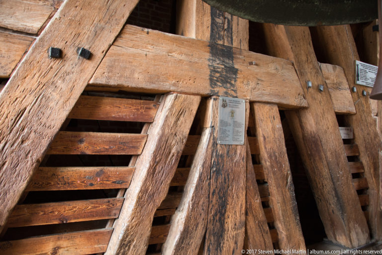Heavy aged timber braces with iron straps and a small identification plaque inside Wawel Cathedral's bell tower.