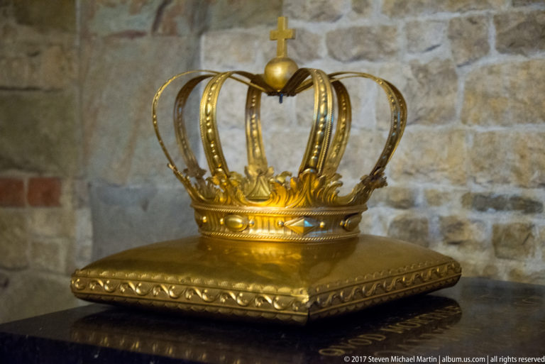 Gilded openwork crown with tall arches, orb, and cross displayed on a square gold cushion.