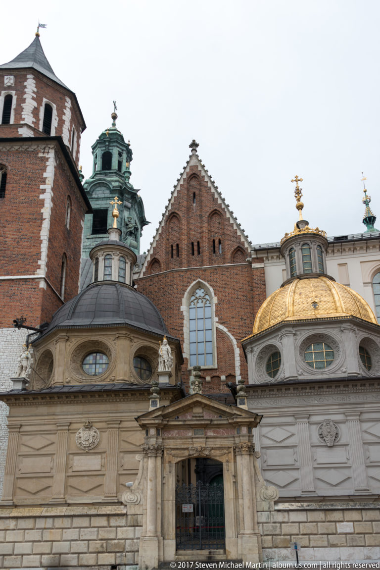 Wawel Cathedral chapels with pale stone façades, a brick gable, green-patinated cupola, and gilded dome.
