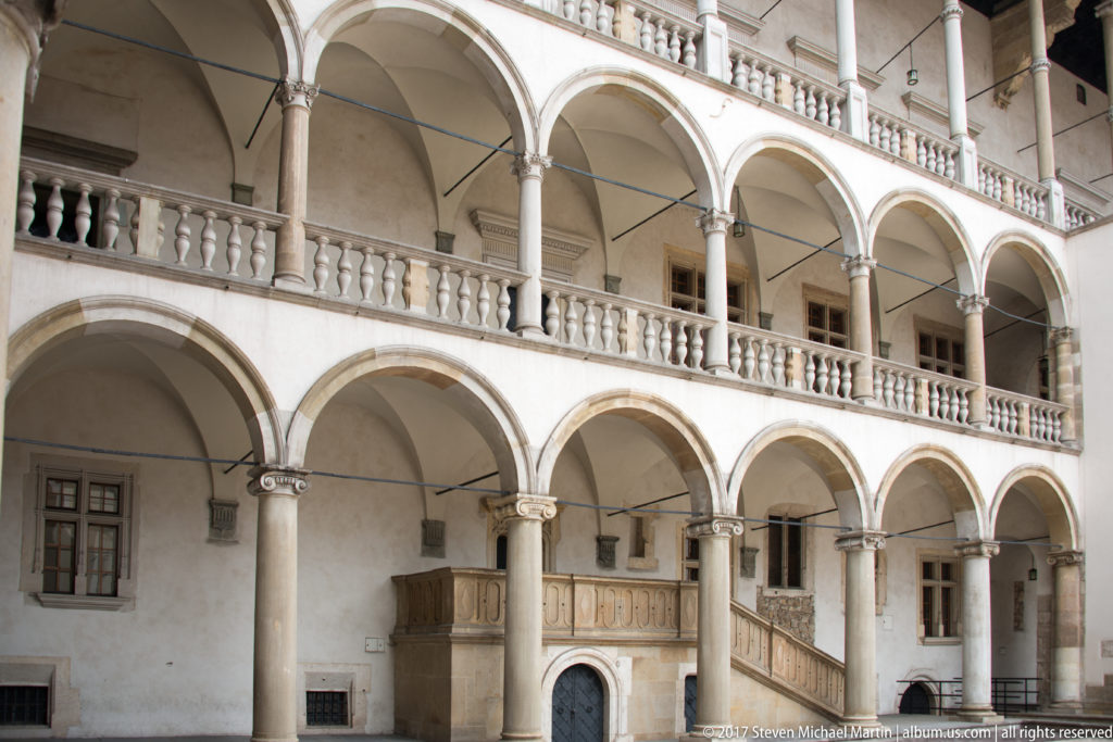 Two levels of white Renaissance arcades with slender columns and balustrades in Wawel Royal Castle's courtyard.