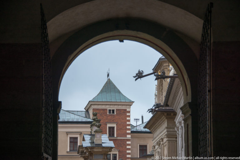 Dark arched passage framing a red-brick tower with a pyramidal roof and adjoining palace façades.