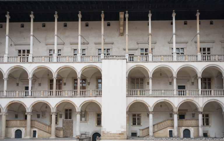 Stacked white arcades, upper columns, balustrades, doors, and stairs on the Wawel Royal Castle courtyard façade.